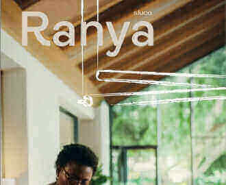 Frau mit Brille arbeitet an einem Tisch in einem modernen Raum mit Holzdecke und Pflanzen im Hintergrund.