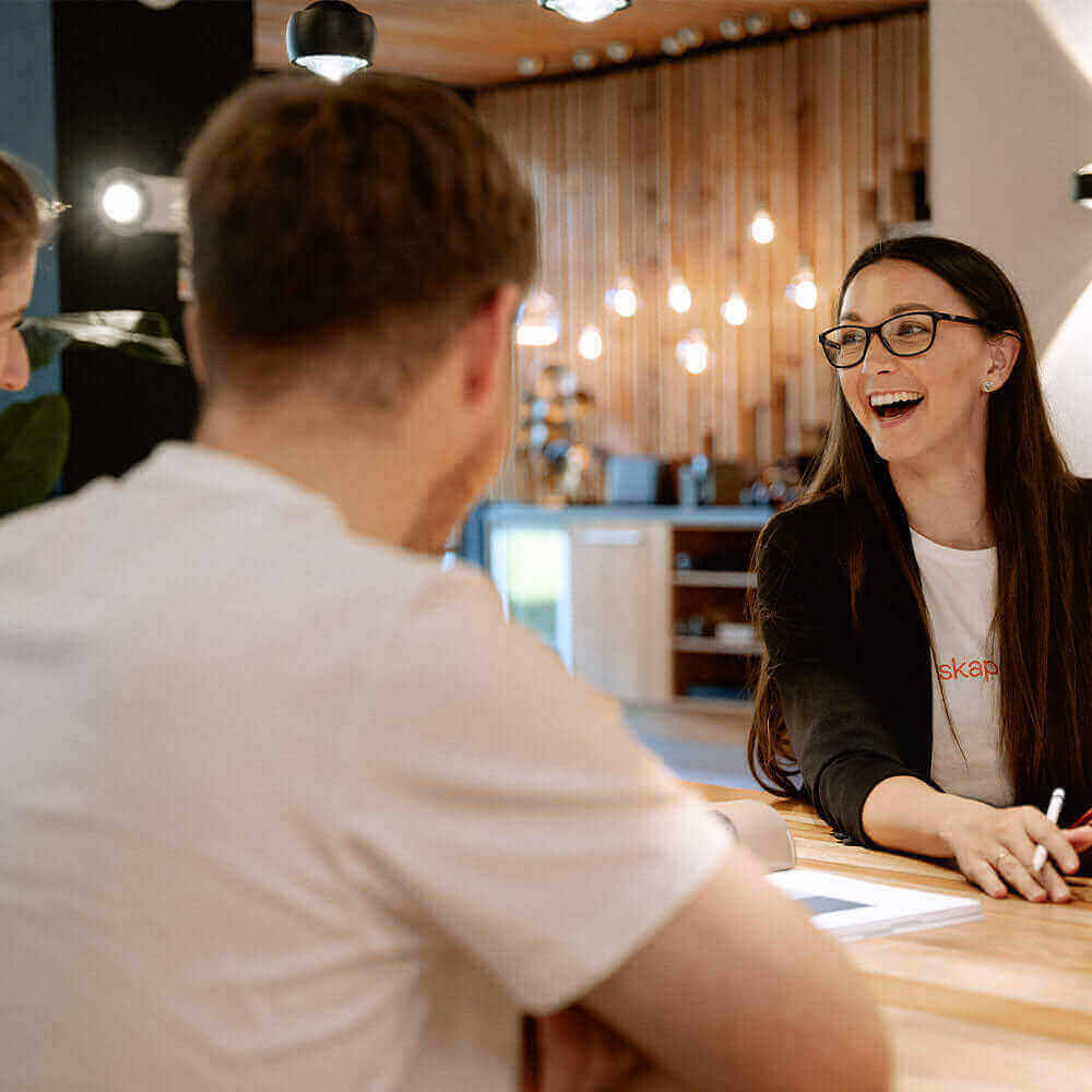 Frau mit Brille lächelt beim Meeting am Tisch, zeigt Engagement und Teamarbeit in modernem Büro