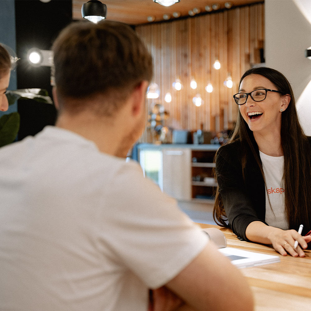 Frau mit Brille lächelt beim Meeting am Tisch, zeigt Engagement und Teamarbeit in modernem Büro