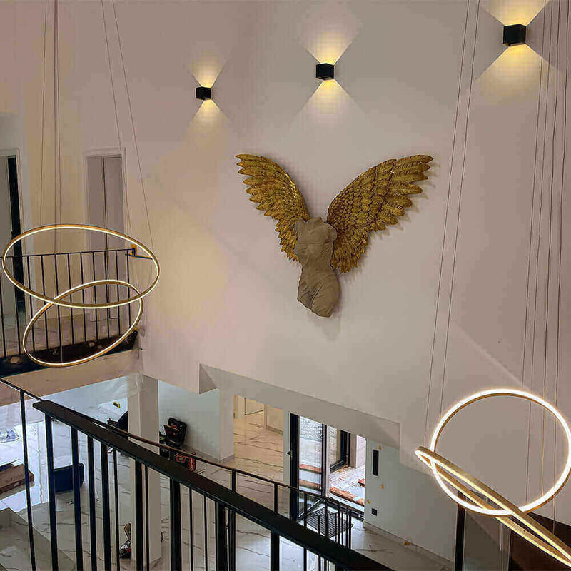 Elegante Innenansicht mit gestalteter Wand und goldenen Engelsflügeln sowie modernen Pendelleuchten.
