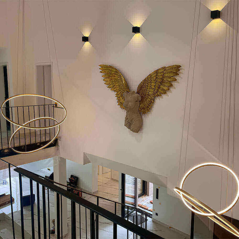 Elegante Innenansicht mit gestalteter Wand und goldenen Engelsflügeln sowie modernen Pendelleuchten.