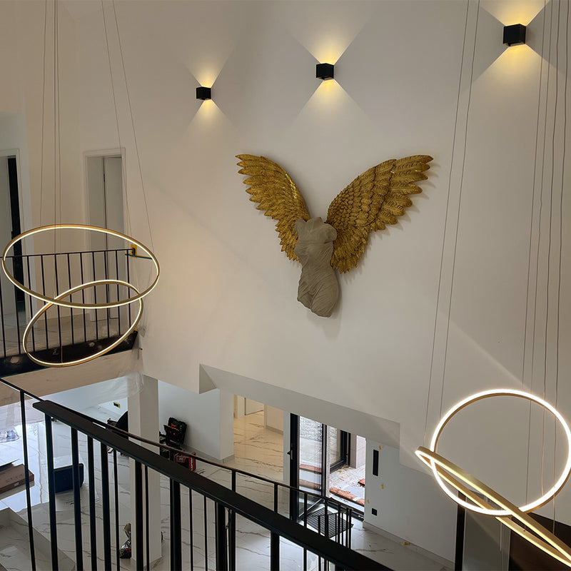 Elegante Innenansicht mit gestalteter Wand und goldenen Engelsflügeln sowie modernen Pendelleuchten.