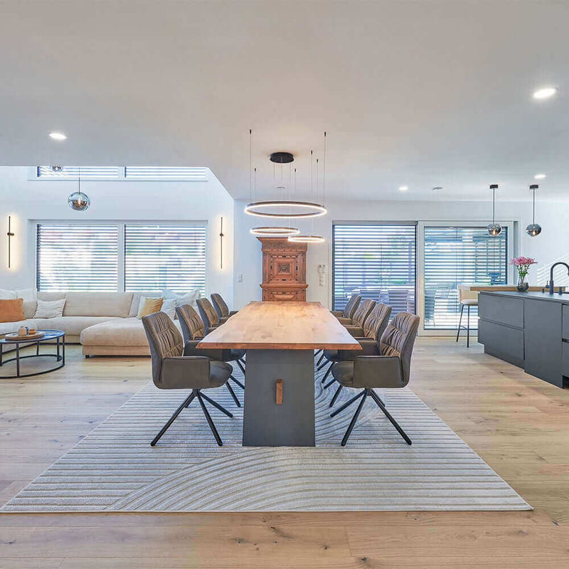 Modern dining room with a large wooden table, stylish chairs, and an open-plan layout featuring a cozy living area.