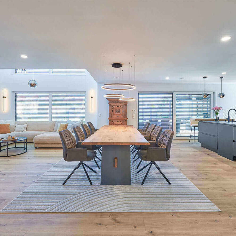 Modern dining room with a large wooden table, stylish chairs, and an open-plan layout featuring a cozy living area.