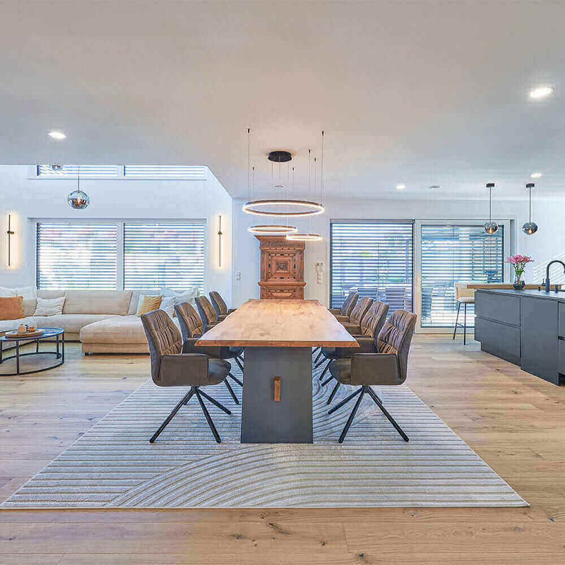 Modern dining room with a large wooden table, stylish chairs, and an open-plan layout featuring a cozy living area.