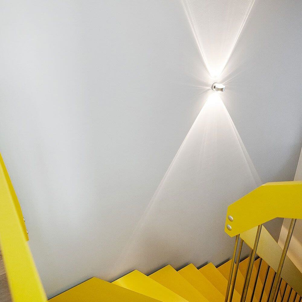 s.luce Beam vägglampa Up & Down med glaslinser på gul trappa med ljusstrålar.