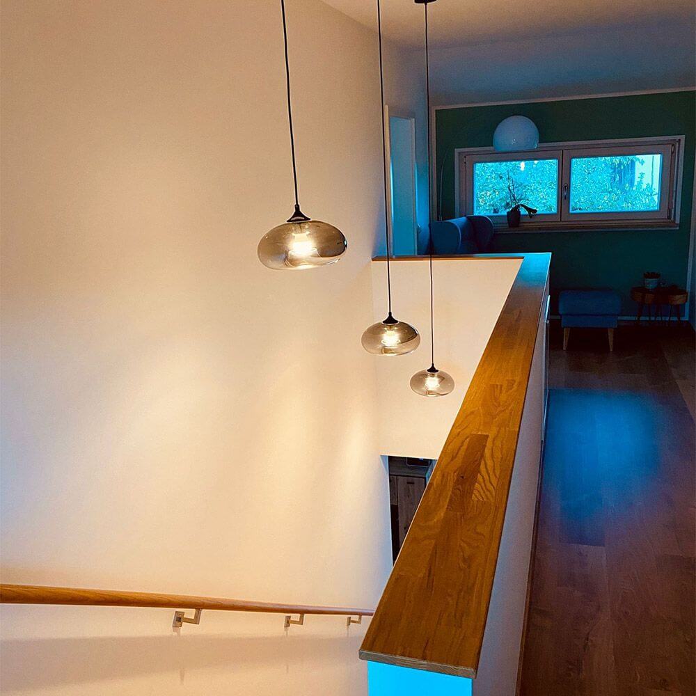 s.luce Cruet Galerie-Pendelleuchte Glas extra lang 5m in einem hellen Treppenhaus mit Holzgeländer.