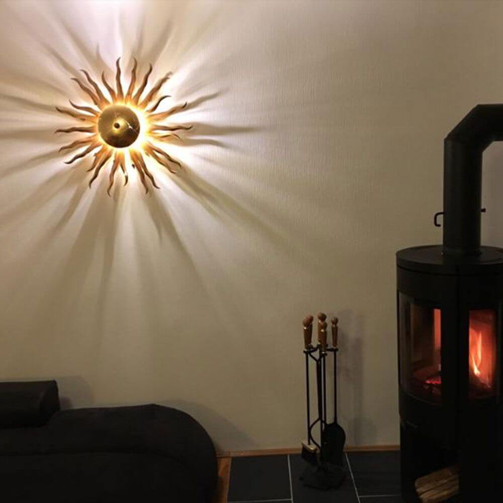 s.luce Diator XL håndsmedet sol i rust- & guldfarver på væg, hyggelig atmosfære med lysleg.