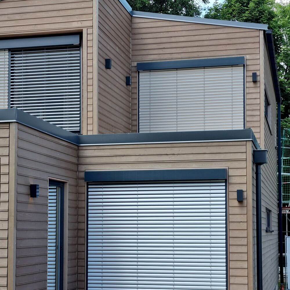 Moderne Fassade eines Hauses mit Holzverkleidung und Aluminiumrollläden.