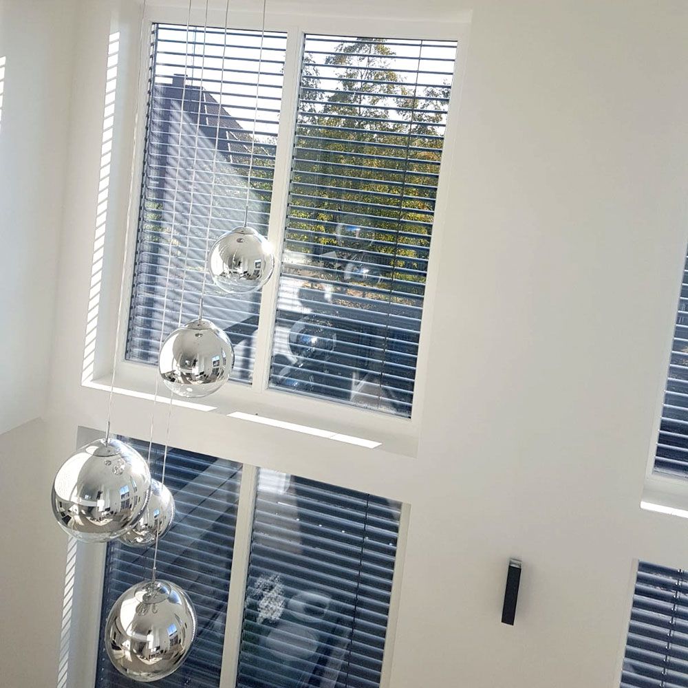 Hängende moderne Leuchten in Silberoptik vor Fenstern mit Jalousien