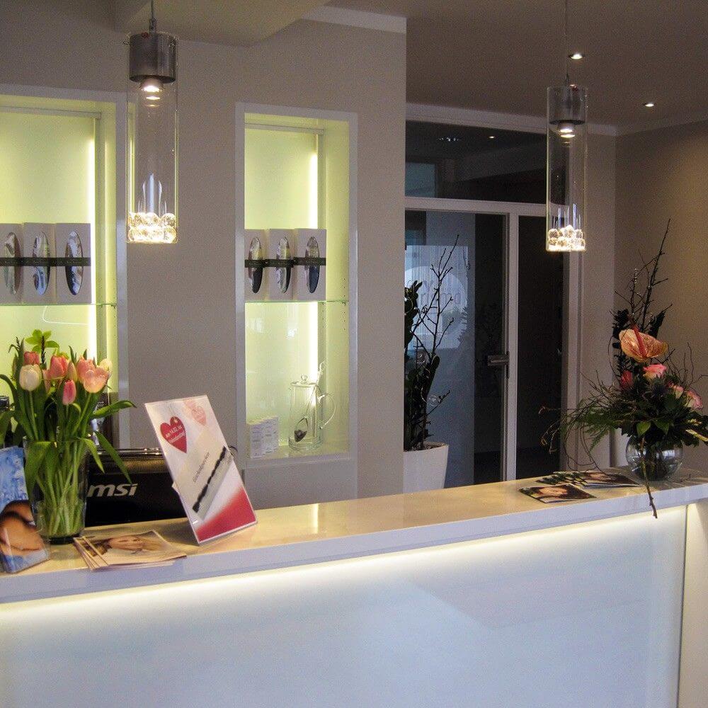 Moderne Empfangstheke mit s.luce MyLight Hängeleuchten und dekorativen Blumenarrangements.