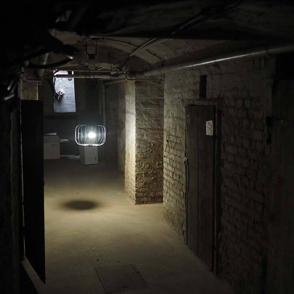 s.luce Rooms Gitter-Hängeleuchte in einem flurähnlichen Raum mit Betonwänden und schwachem Licht.