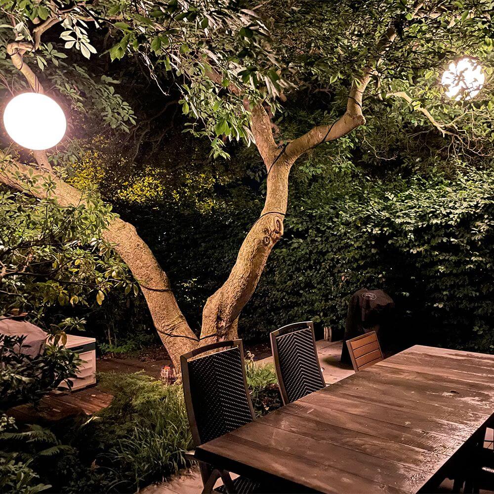 s.luce Globe Hänge-Kugellampe für Innen & Außen IP54 aufgehängt in einem Garten mit Tisch.