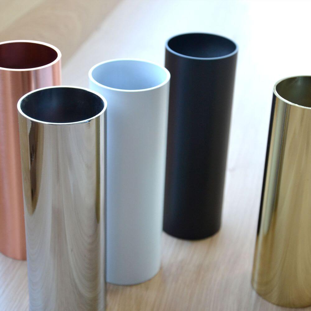 Fünf dekorative Zylinder in verschiedenen Farben: Kupfer, Silber, Weiß, Schwarz und Gold auf Holzuntergrund.