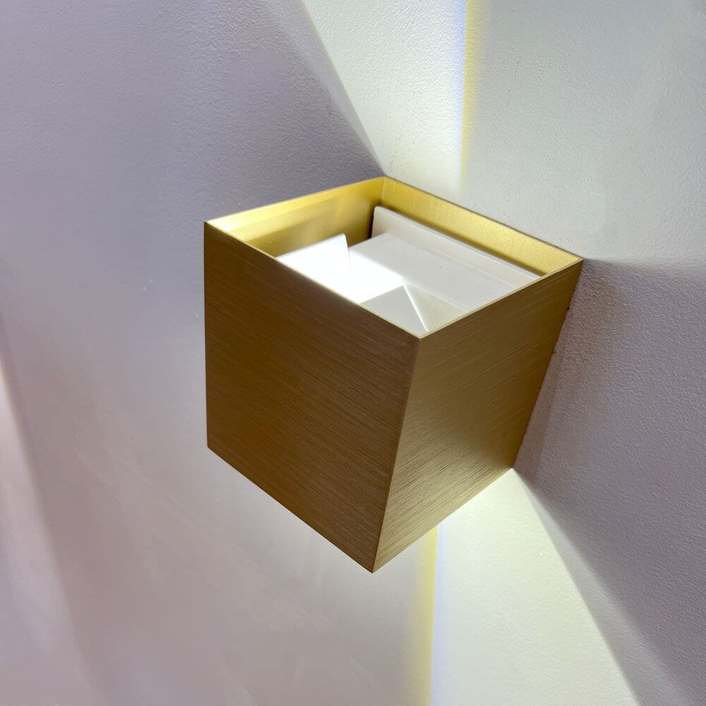 Candeeiro de parede LED Ixa com cobertura quadrada em design moderno, na cor dourada, montado numa parede.