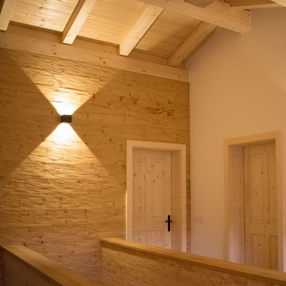 s.luce Ixa LED Wandlampe mit Bewegungsmelder leuchtet an einer Holzwand im Flur.