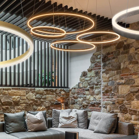 s.luce LED Ring Pendellampe Ø 100cm im modernen Wohnzimmer mit Steinwänden und stilvollem Sofa.