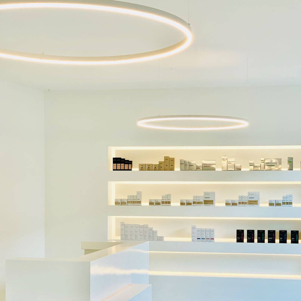s.luce Lampe suspendue en anneau LED dans une pièce moderne, éclairage minimaliste au-dessus des étagères avec des produits cosmétiques.