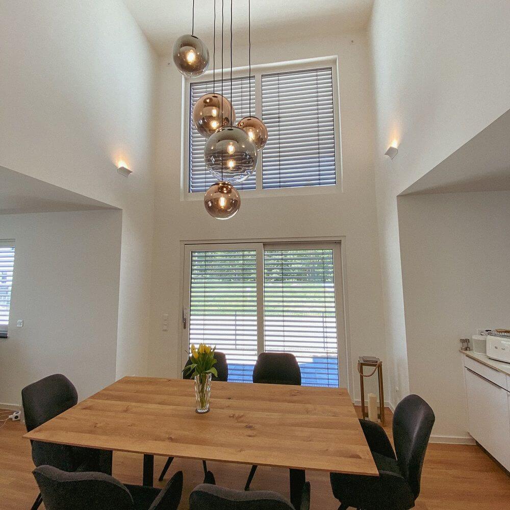 Moderne Galerieleuchte mit Glaskugeln in einem hellen Esszimmer über einem Holztisch.
