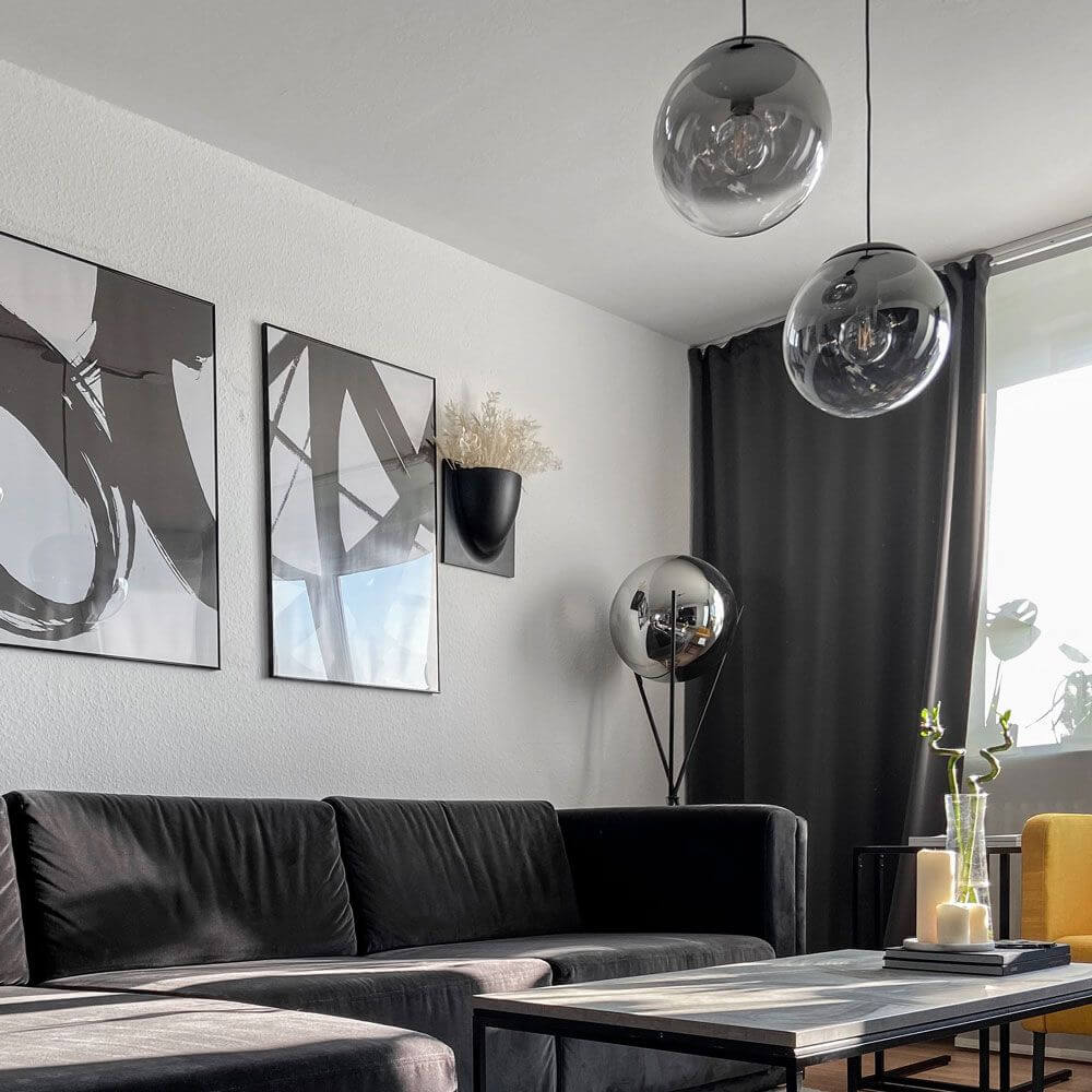 Moderner Wohnraum mit s.luce Progress Pendelleuchten in Glas und zeitgemäßer schwarzer Couch.