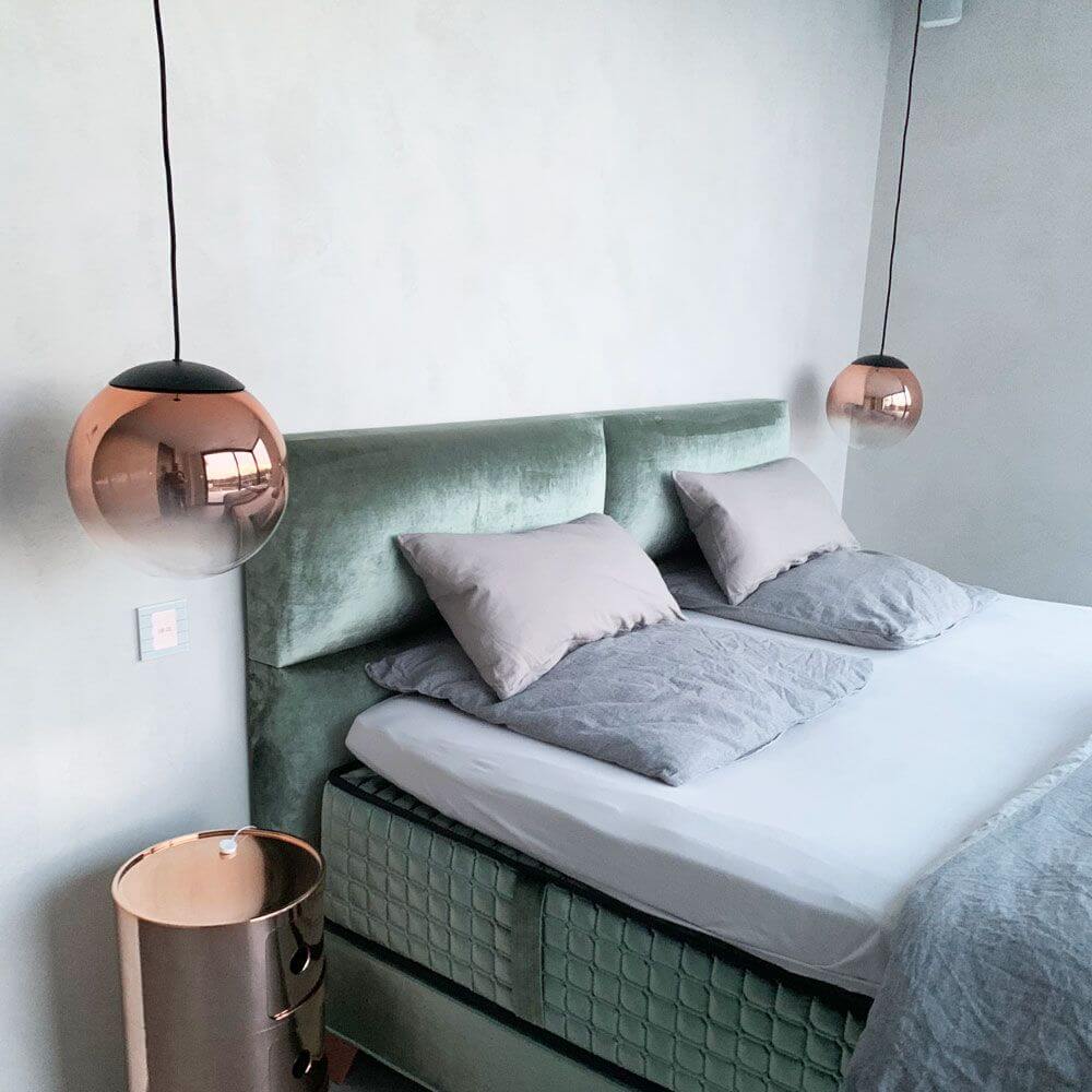 Moderne s.luce Progress Pendelleuchte in Glas mit Farbverlauf über einem stilvollen Bett im Schlafzimmer.