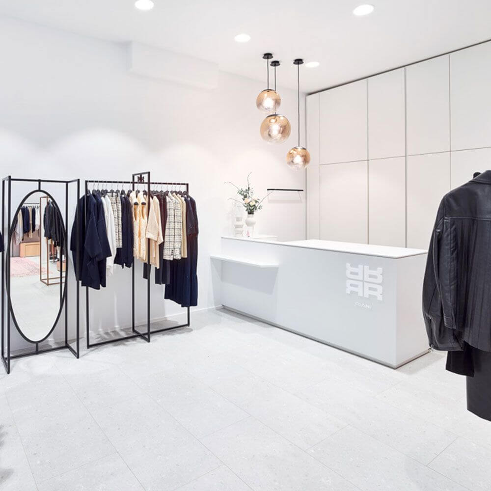 Modernes Bekleidungsgeschäft mit eleganter Garderobe, Empfangstresen und stilvollen Lampen.
