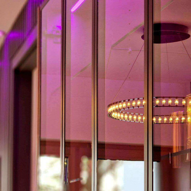Reflektierende Scheiben mit lila Beleuchtung und modernem Kronleuchter im Hintergrund.