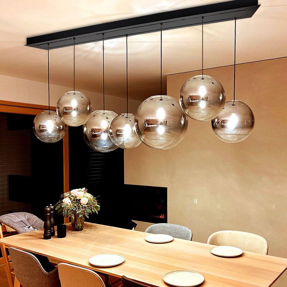 s.luce dosel modular en forma rectangular con varias lámparas esféricas colgantes sobre una mesa de comedor.