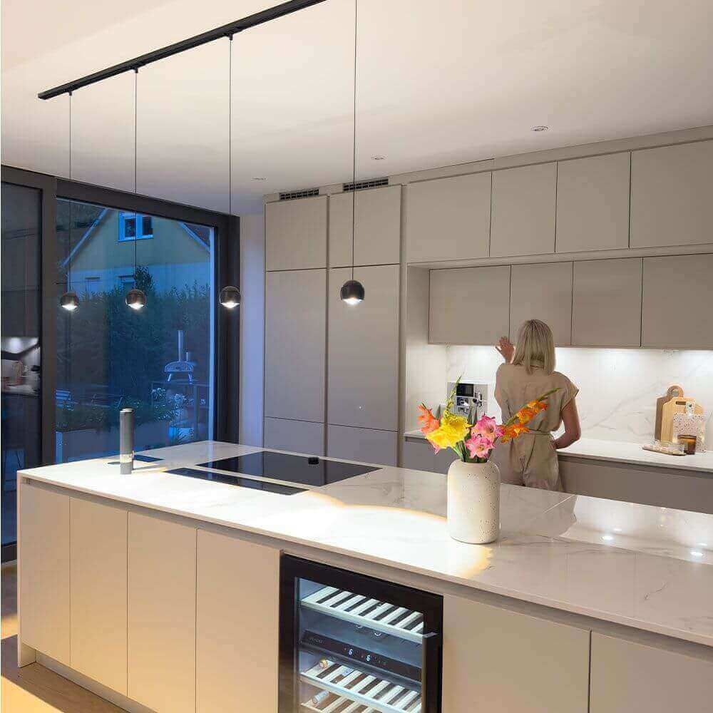 Moderne Küche mit Insel und Pendelleuchten, eine Frau bereitet etwas vor.