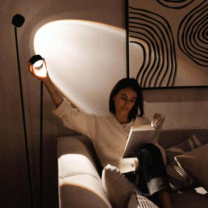 Frau sitzt auf der Couch und liest ein Buch, während sie eine Lampe mit sanftem Licht hält.