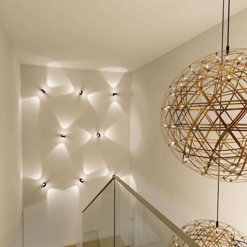 s.luce Beam Wandleuchte Up & Down mit Glaslinsen an einer Treppe mit dekorativen Wandlichtern.