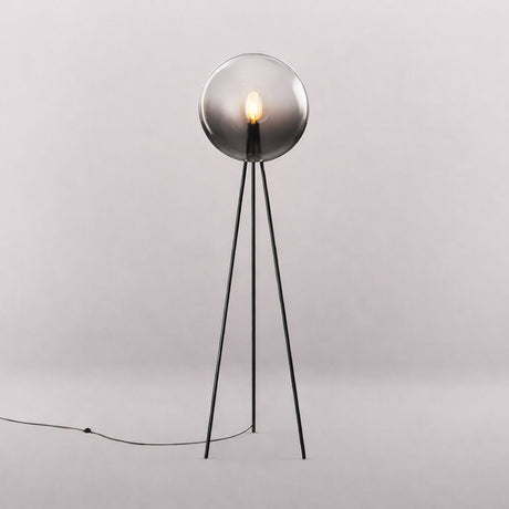 s.luce Dreibein-Stehleuchte Orb Tripod 160cm mit Glaskugel steht in einem Raum, strahlt sanftes Licht aus.