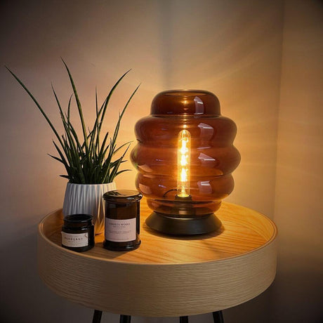 s.luce Echos Glas Tischleuchte E27 mit Schalter auf einem Holztisch neben Kerzen und Pflanze.