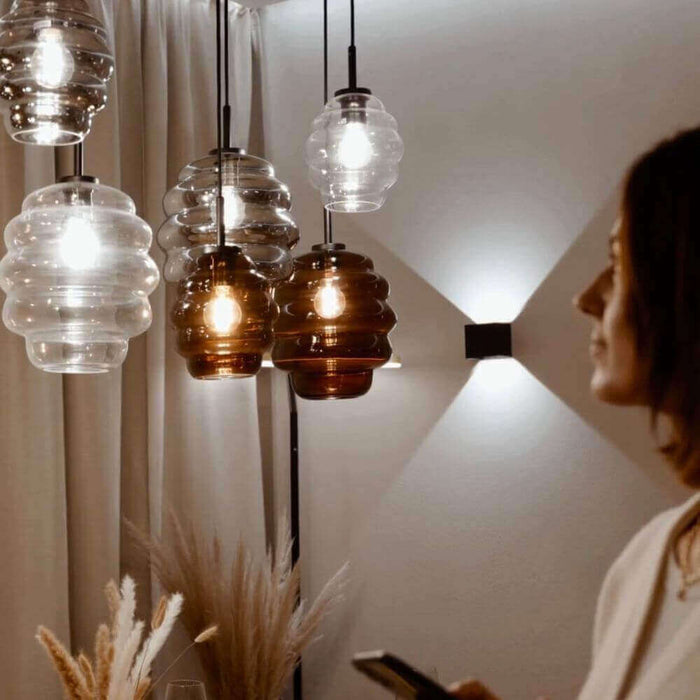 Moderne Hängeleuchten in warmem Licht mit dekorativem Glasanhänger, Frau betrachtet das Design.