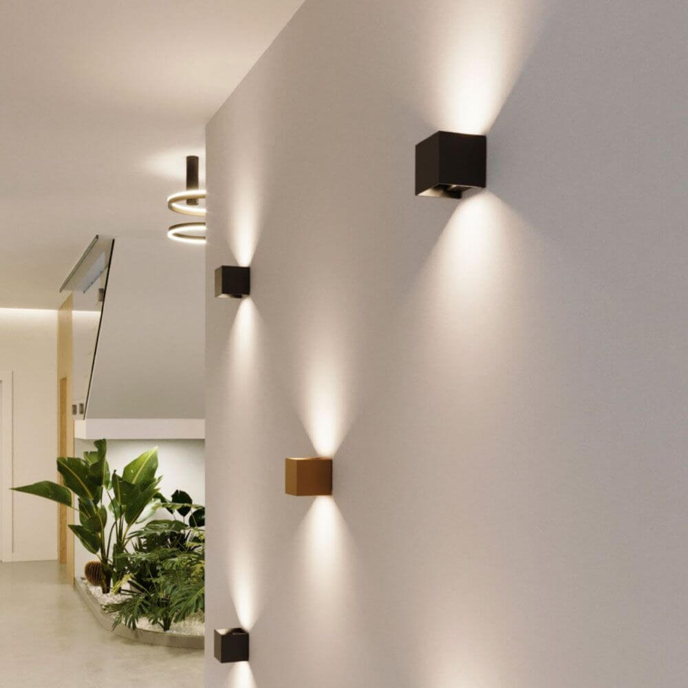Moderne Ixa LED-Wandleuchten in quadratischer Form an einer Wand, schwarz und gold, im stilvollen Innenraum.