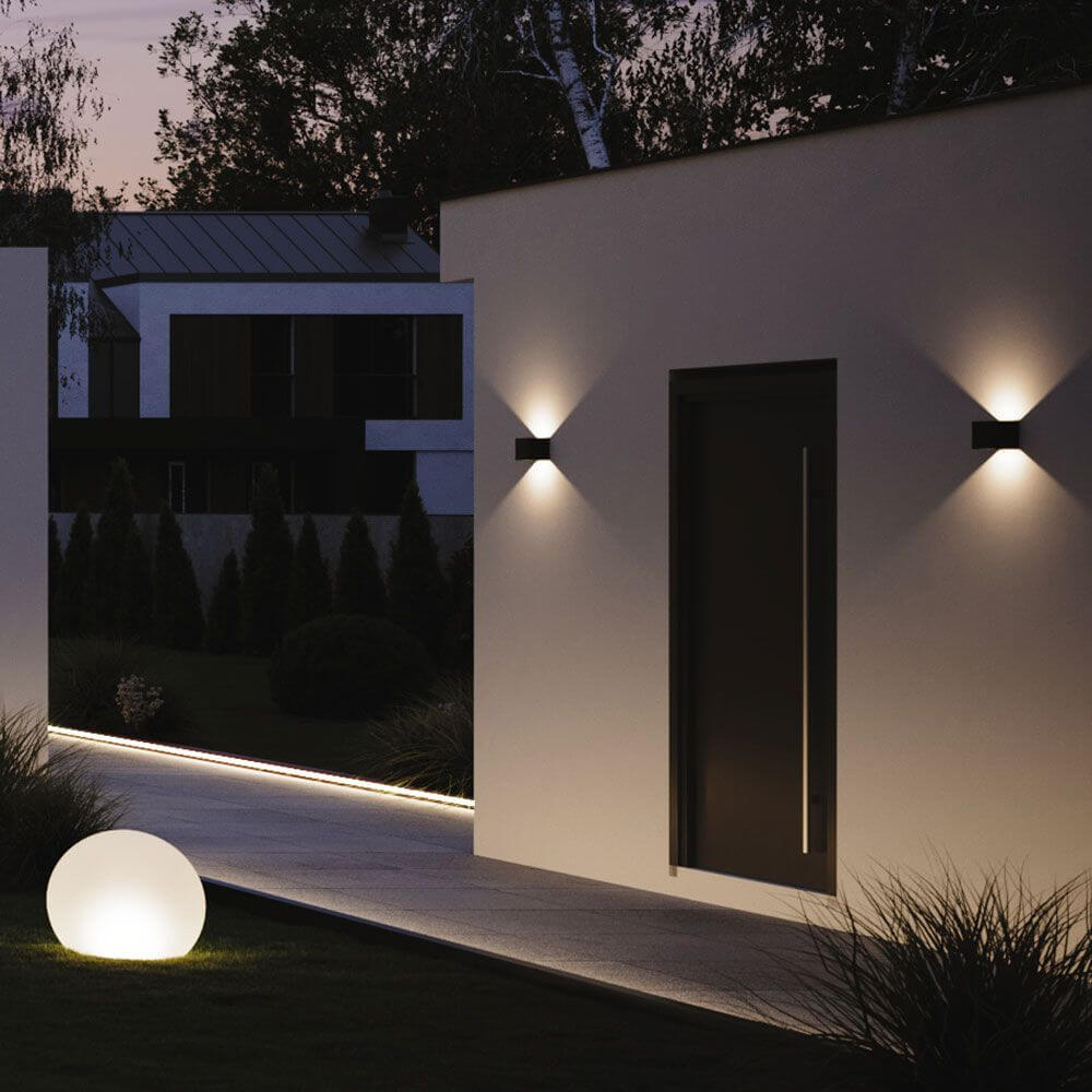Moderne Ixa LED-Wandleuchten an einer Hauswand bei Nacht, strahlend und stilvoll in einem Garten.