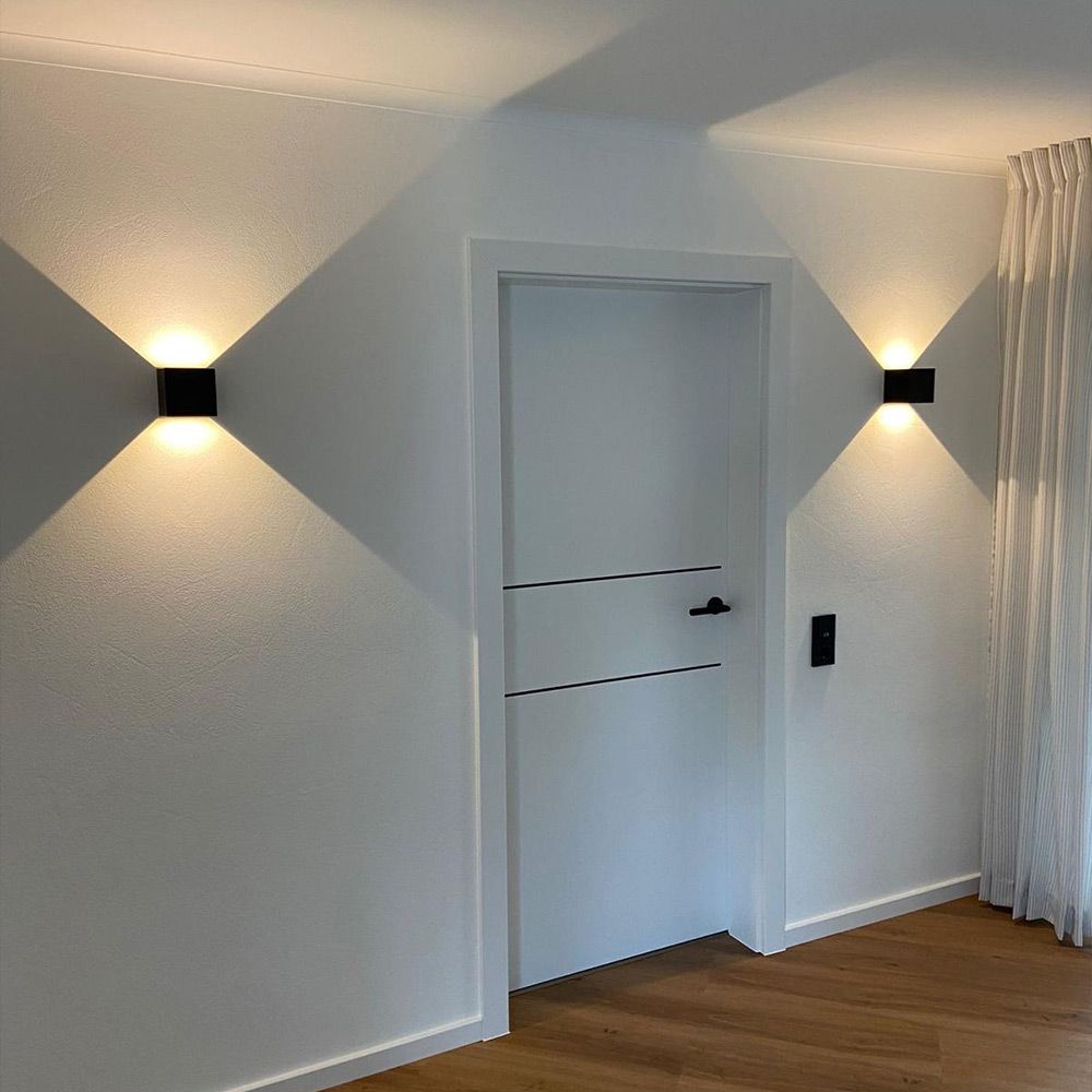 Moderne Ixa LED-Wandleuchte mit quadratischer Abdeckung an einer weißen Wand, Schattenmuster erzeugend.