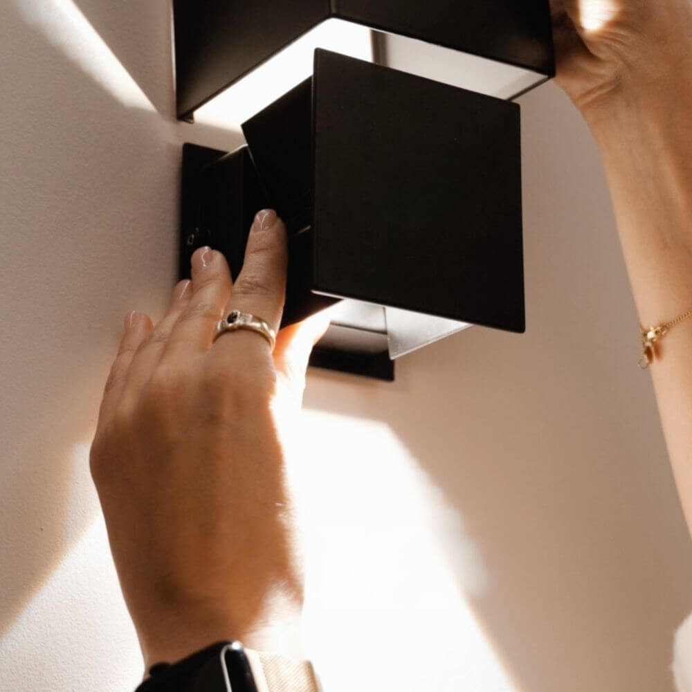 Nahaufnahme einer Hand, die eine moderne schwarze Wandlampe an der Wand befestigt.