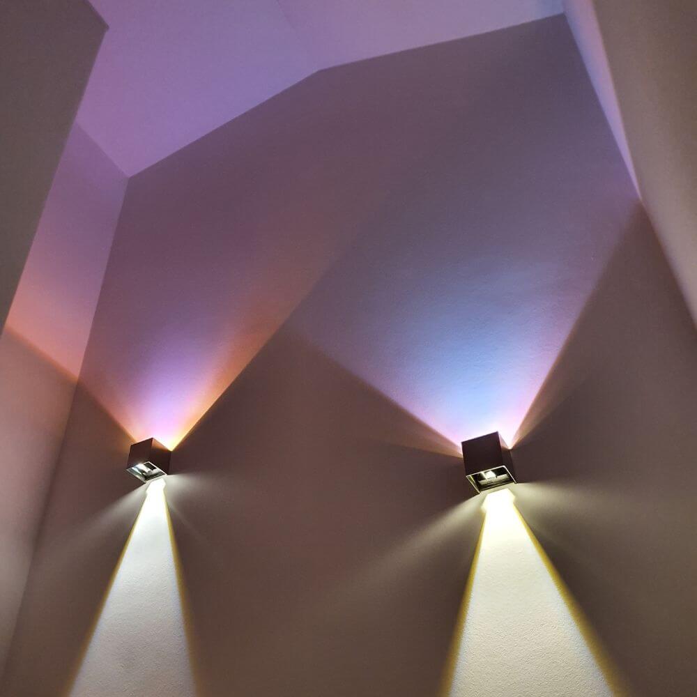 s.luce Ixa LED Wandlampe in einem modernen Innenraum mit verstellbarem Lichtkegel und bunten Farbspielen.