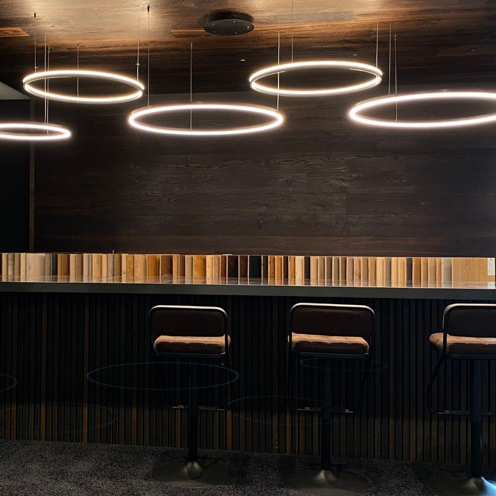 s.luce LED Ring Hängeleuchte 5-flammig Exzentrisch über einer modernen Bar mit Holzdetails.