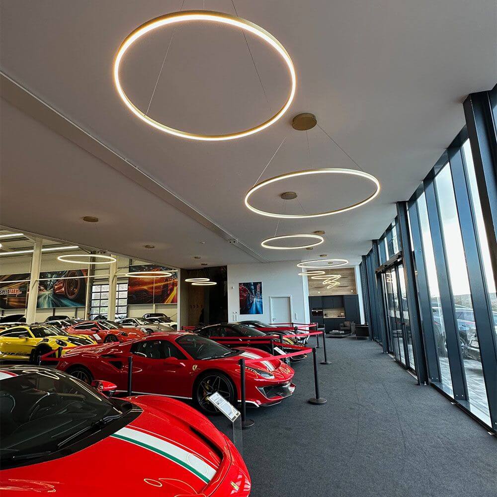 s.luce LED Ring Pendelleuchte rund Direkt oder Indirekt in einer modernen Autoausstellung mit roten Sportwagen.