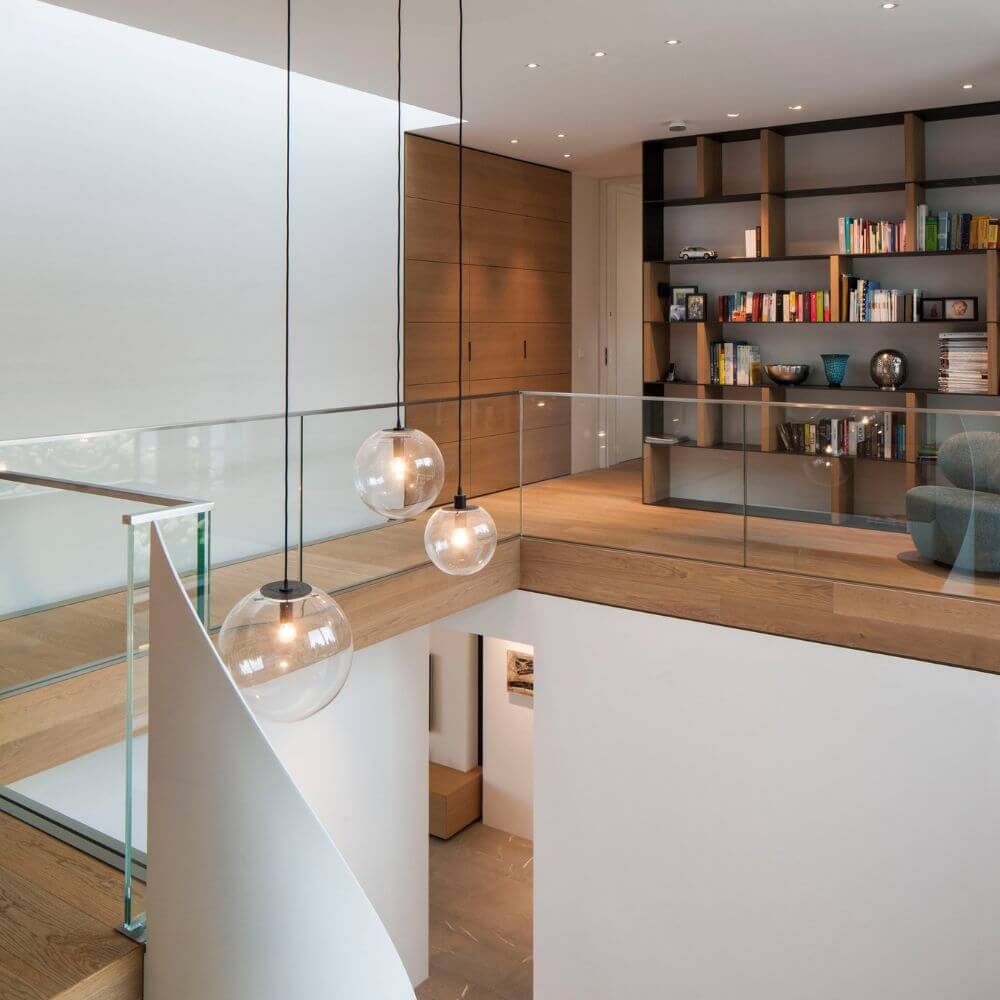 s.luce Orb Glaskugel Hängeleuchte in modernem Wohnbereich mit Holzregalen und Glasbalustrade.