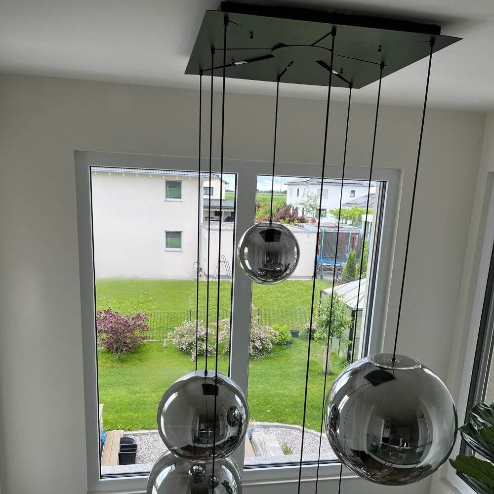 s.luce Orb XL Galerieleuchte 8-flammig mit Modular Baldachin über einem Fenster mit Gartenblick.
