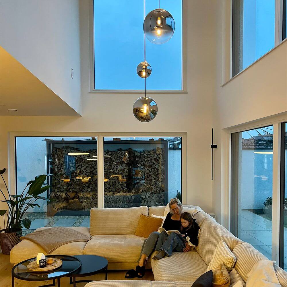 Moderne Galeriebeleuchtung mit Glaskugeln in elegantem Wohnzimmer mit großen Fenstern und gemütlicher Couch.