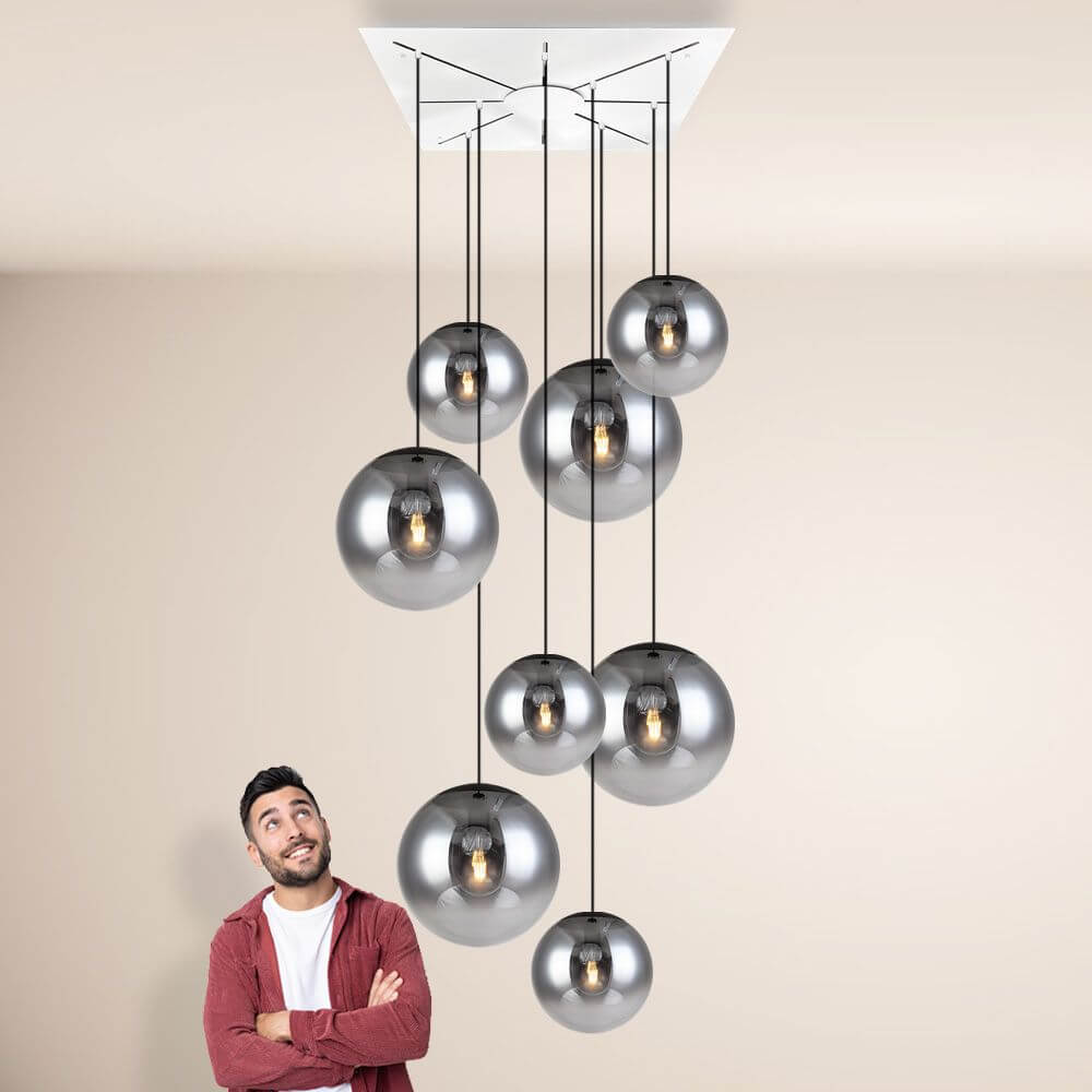 s.luce Progress XL Galerieleuchte 8-flammig mit Modular Baldachin hängt mit eleganten Glaskugeln über einem staunenden Mann.