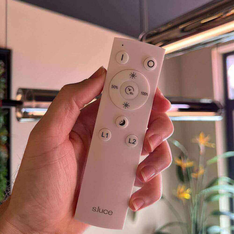 Hand hält eine moderne Fernbedienung von s.luce zur Steuerung von Beleuchtung.