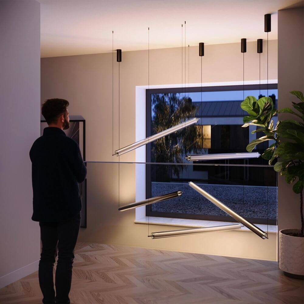 Mann betrachtet moderne hängende Beleuchtung in einem stilvollen Raum mit Fenster und Pflanzen.