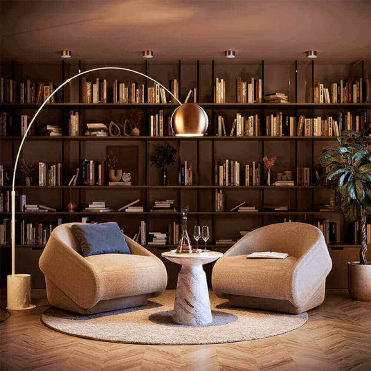 Gemütliche Sitzecke mit modernen Stühlen, Tisch und Bücherregal im Hintergrund, warmes Licht sorgt für einladende Atmosphäre.