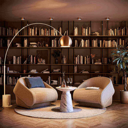 Gemütliche Sitzecke mit modernen Stühlen, Tisch und Bücherregal im Hintergrund, warmes Licht sorgt für einladende Atmosphäre.