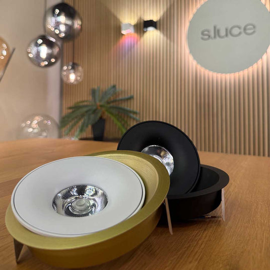 Moderne Einbauleuchten von s.luce in Gold, Weiß und Schwarz auf einem Holztisch, ideal für stilvolle Raumbeleuchtung.